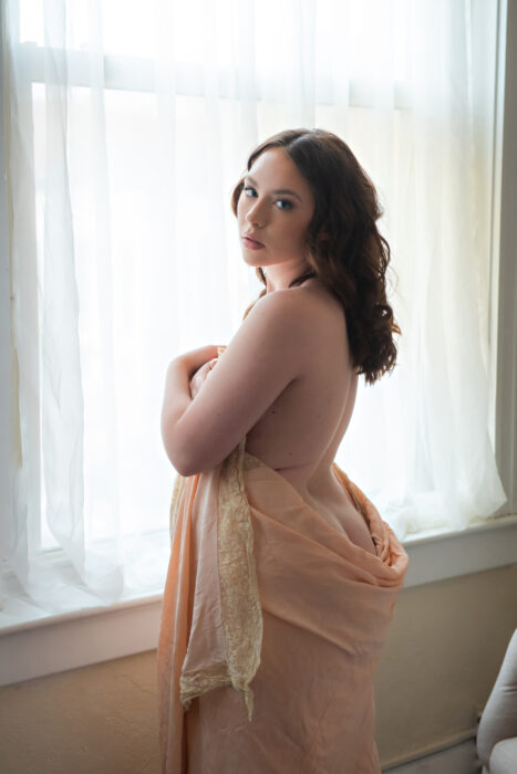 Boudoir portrait of a woman at  window, wrapped in a sheet. 